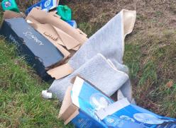 cardboard boxes and carpet fly tipped on the side of a verge